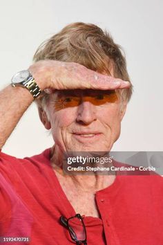 an older woman in red shirt holding her hands up to her face and looking at the camera