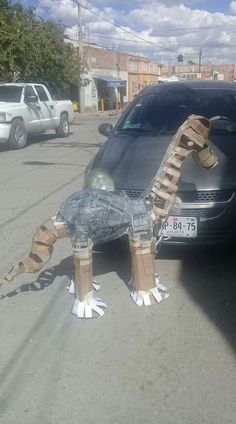 an animal made out of cardboard sitting on the side of a road next to a car