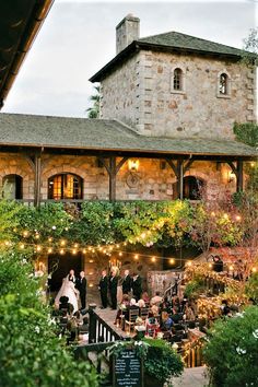 an outdoor wedding venue with string lights and greenery on the outside, surrounded by stone buildings