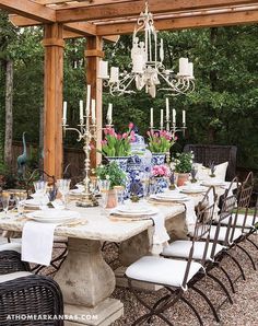 an outdoor dining table with chairs and chandelier hanging from the wooden pergoline