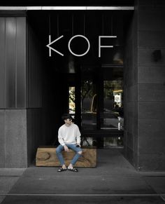 a man sitting on top of a wooden bench in front of a kof store