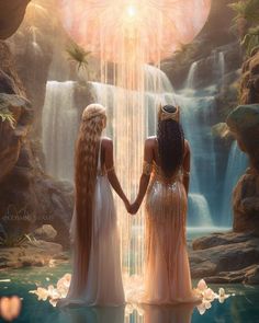 two beautiful women standing in front of a waterfall holding hands and looking at each other