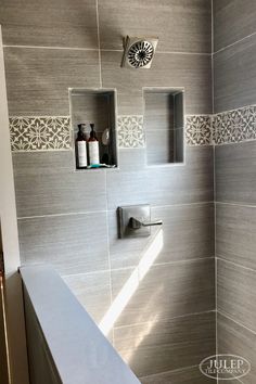 a bathroom with gray tile and white fixtures on the shower wall, along with soap dispensers