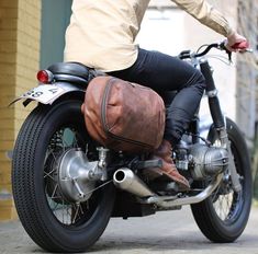 a man riding on the back of a motorcycle with a brown bag strapped to it's seat