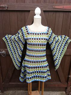 a crocheted top on a wooden stand in front of a wood wall and fence