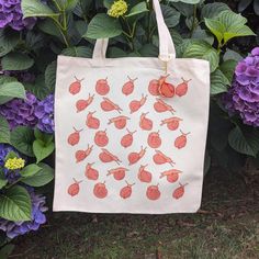 a white bag with red snails on it sitting in front of purple flowers