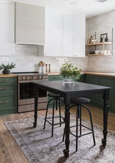 a kitchen with green and white cabinets, an area rug and two stools in front of the counter