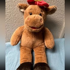 a brown stuffed cow with a red bow on its head sitting on a blue blanket