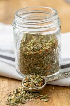 a glass jar filled with herbs sitting on top of a wooden table next to a spoon