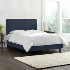 a bed with white sheets and blue headboard in a room next to a window