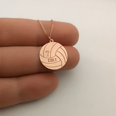 a person's hand holding a gold pendant with a volleyball ball on it