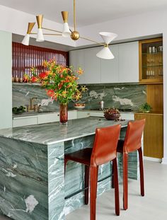 a kitchen with marble counter tops and red chairs in front of an island that has flowers on it