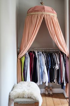 a bed with a canopy over it and lots of clothes hanging on the rails in front of it