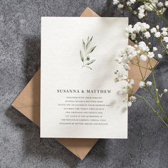 the wedding stationery is laid out on top of an envelope and some flowers are next to it