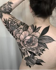 a woman's back tattoo with flowers and leaves on her upper arm, which is black and white