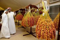 two men standing next to each other in front of some fruit hanging from hooks on poles