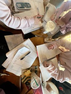 two girls are doing homework at a table with cups and papers on top of them