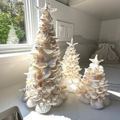 two small christmas trees made out of seashells on a table next to a window