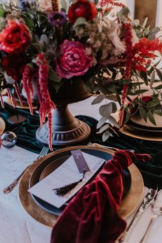 the table is set with red and pink flowers, silverware, and napkins