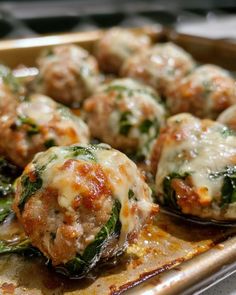 meatballs covered in cheese and spinach are on a baking sheet, ready to be eaten