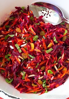 a white bowl filled with red cabbage and almonds next to a silver serving spoon