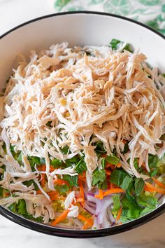 a salad with shredded cheese and vegetables in a black bowl on a white tablecloth