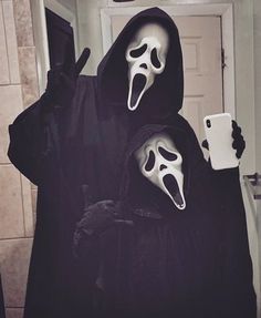 two people dressed up in halloween costumes with ghost masks on their faces and one holding a cell phone