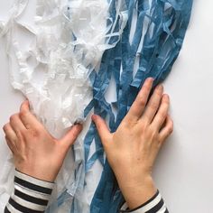 two hands reaching for something on top of a white surface covered in blue and white tissue paper