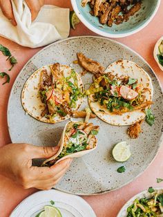 three fish tacos on a plate with limes, cilantro and onions