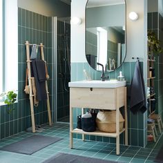 a bathroom with green tiles and a white sink under a large mirror on the wall