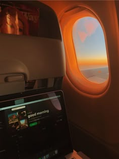 an airplane window looking out at the sky and clouds, with a laptop on it