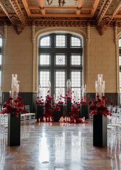 a large room filled with lots of tall black vases covered in red flowers and candles