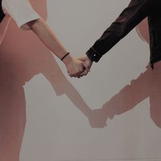 two people holding hands in front of a pink wall with the shadow of one person's hand