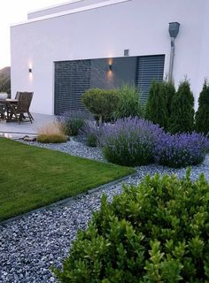 an outdoor patio area with gravel, grass and shrubs in front of a white building