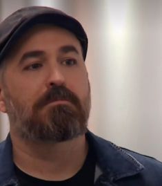 a man with a beard wearing a denim jacket and hat looking off to the side