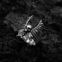 The Nocturnus Bane Vampire Ring. Wickedly crafted to perfection, this stunning ring features intricate vampire wings that wrap around your finger in an eternal embrace. Cast from high-quality sterling silver, the ring's dark luster and detailed texture offer a touch of enigmatic chaos to any ensemble. It is ideal for vampiric and gothic fashion enthusiasts or as a unique gift for those who revel in fantasy and mystique. Wear it as a symbol of your fearless spirit and fly high on the wings of dar Gothic Winged Jewelry Gift, Gothic Winged Jewelry For Gifts, Silver Winged Fantasy Jewelry, Silver Fantasy Wing-shaped Jewelry, Silver Wing-shaped Fantasy Jewelry, Fantasy Silver Wing-shaped Jewelry, Gothic Sterling Silver Rings, Gothic Skull Open Ring Gift, Elegant Silver Skull Ring For Halloween