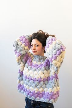 a woman wearing a multicolored sweater is covering her head with her hands while standing in front of a white wall