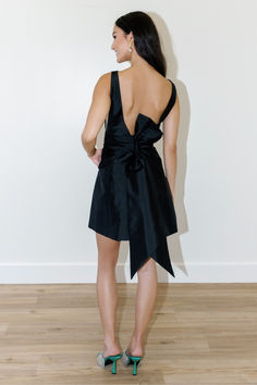 the back of a woman in a short black dress with a bow at the waist