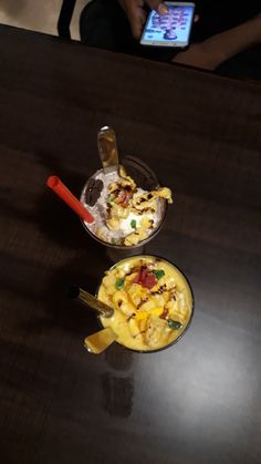 two bowls of food sitting on top of a wooden table next to a cell phone