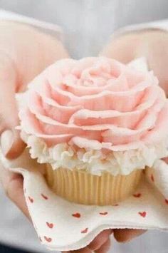 a person holding a cupcake with pink frosting