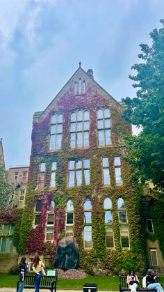 people sitting on benches in front of an old building with ivy growing all over it