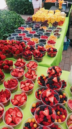 there are many bowls of strawberries and other fruits on the table at this outdoor market