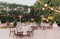 an outdoor wedding reception with white linens and lights strung from the trees, surrounded by greenery