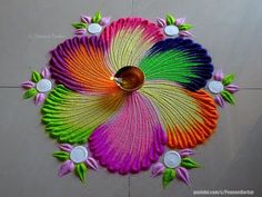 a colorful flower design made with yarn and buttons on the floor in front of a white wall