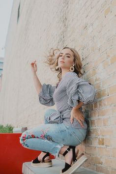 a woman leaning against a brick wall with her hair blowing in the wind and wearing high heels