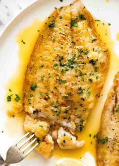 two pieces of fish on a white plate with lemon wedges and parmesan cheese