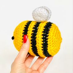 a woman's hand holding a yellow and black knitted purse with a white ball on top