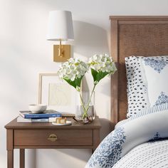 a bed with white flowers in a vase next to a night stand