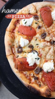 a pizza with tomatoes, olives and mozzarella on it sitting on a black plate