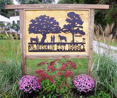 a wooden sign sitting in the middle of a lush green field next to flowers and trees